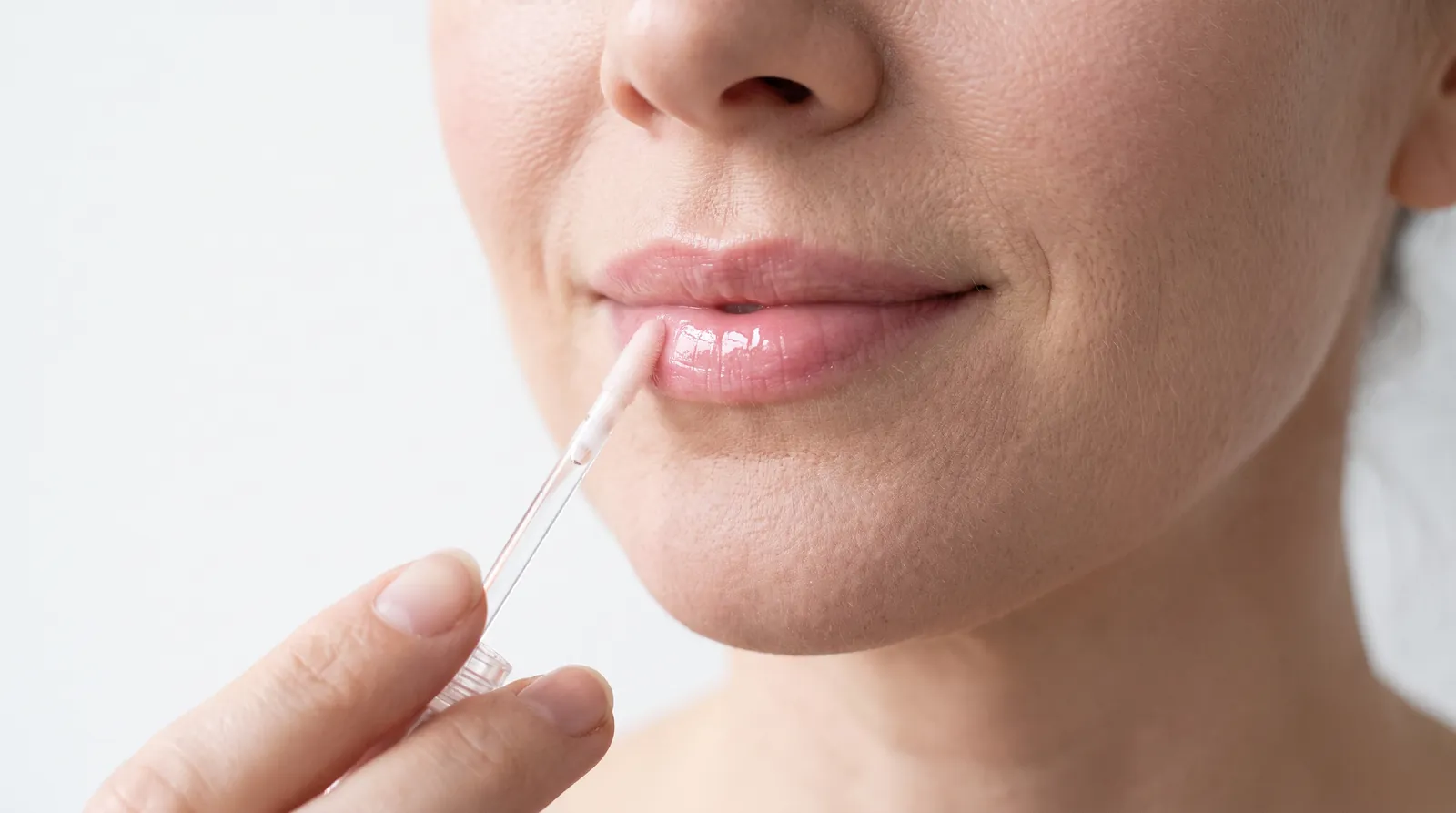 Close de lábios com gloss rosado translúcido sendo aplicado com aplicador